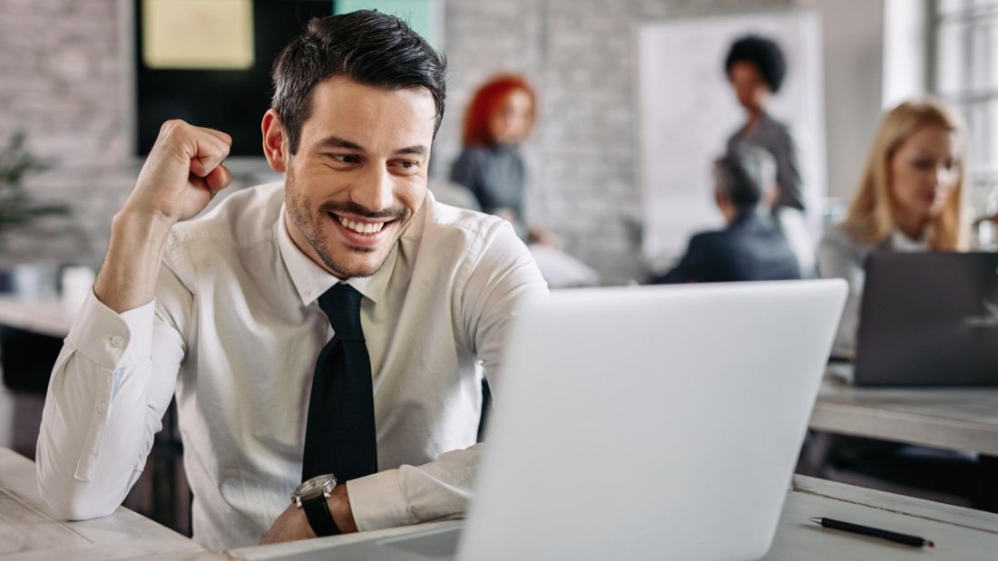 young-happy-businessman-using-computer-office-celebrating-good-news-there-are-people-background