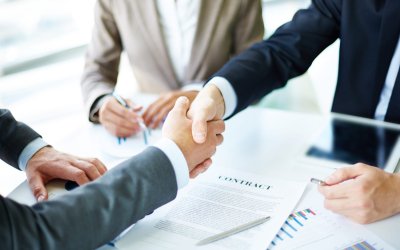 Image of business partners handshaking over business objects on workplace